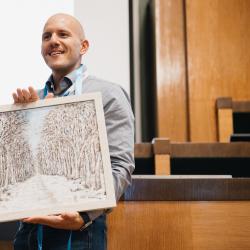 Person holding a painting, in an auditorium