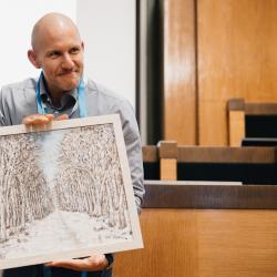 Person holding a painting, in an auditorium