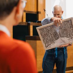 Person holding a painting, in an auditorium