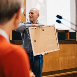 Person holding a painting, in an auditorium
