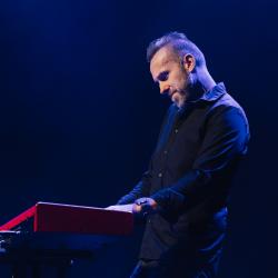 Person playing a keyboard on a dark stage, lit up by stage lights