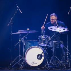 Person playing drums on a dark stage, lit up by stage lights