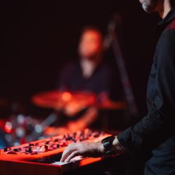 Person playing a keyboard on a dark stage, lit up by stage lights