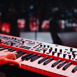 Person playing a keyboard on a dark stage, lit up by stage lights