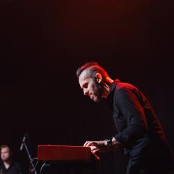 Person playing a keyboard on a dark stage, lit up by stage lights