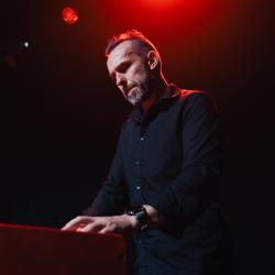 Person playing a keyboard on a dark stage, lit up by stage lights
