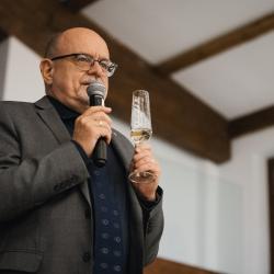 Man speaking to a microphone, holding a glass of champagne